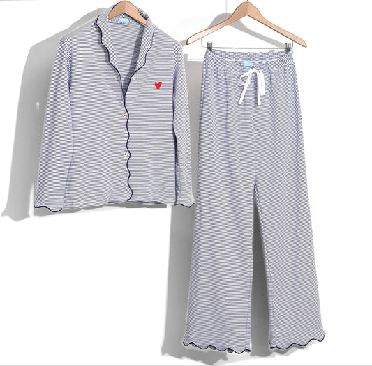 A two-piece women's pajama set with a long-sleeve button-front top and matching wide-leg pants, featuring fine blue and white stripes, scalloped edges, and a small red heart on the chest. The set is displayed on wooden hangers against a white background.